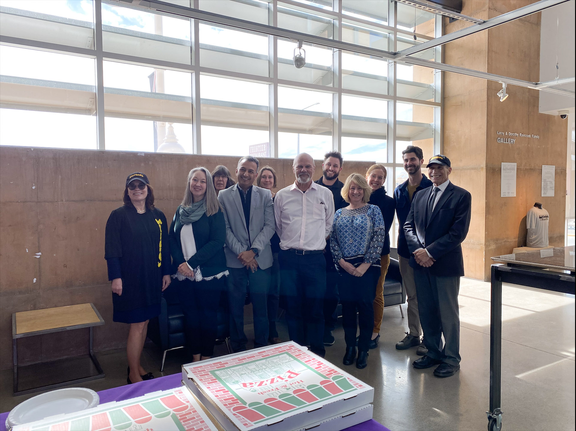 Group of people standing behind a table with pizza boxes